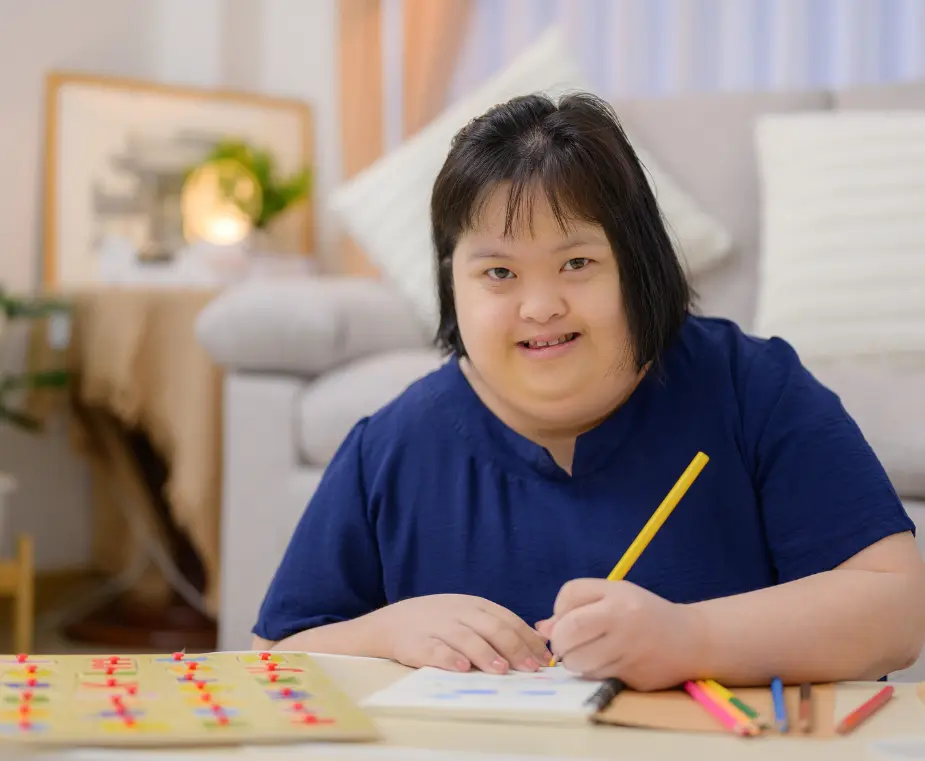 Happy disabled girl smiling at camera while drawing at desk on notepad